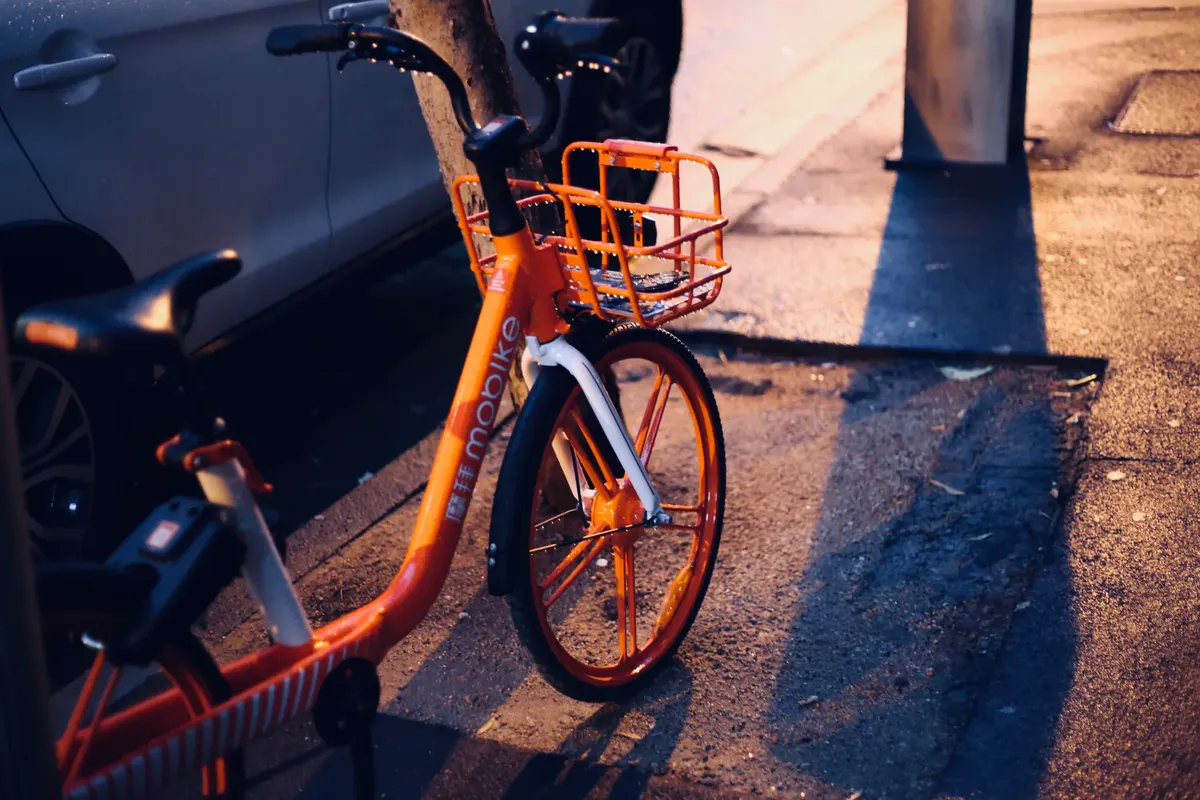 夕方の市街地で、濡れた舗装道路に反射がある明るいオレンジ色の自転車が停まっている