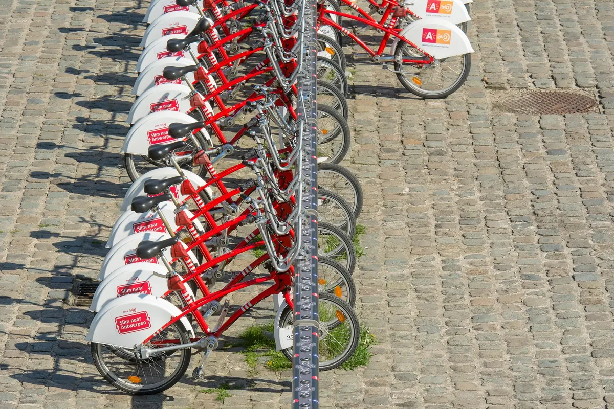 A line of red rental bicycles parked on a cobblestone street, ready for urban transportation.