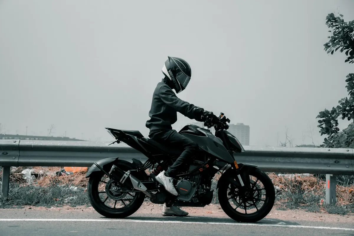 Side view of a motorcyclist wearing a helmet, riding a sports bike on an urban roadside.