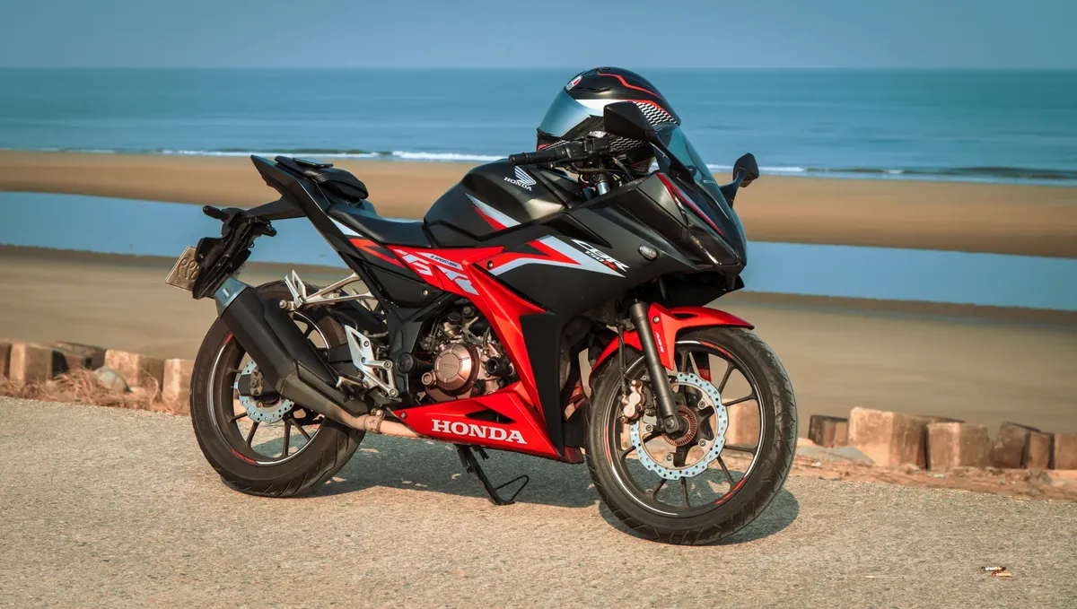 A red and black Honda CBR150R sport bike parked near a beachside roadway.
